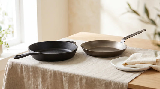 Cast iron skillet and carbon steel skillet side by side on a linen-covered light wood table
