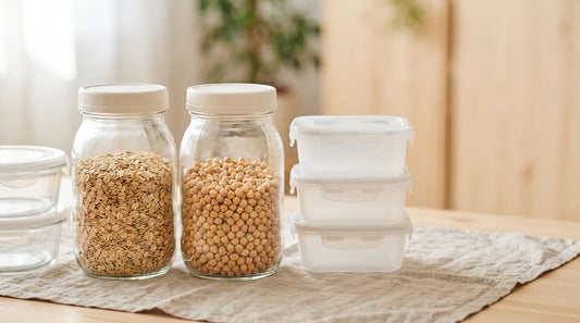 Clear glass wide-mouth storage jars and frosted plastic food storage containers side by side on a linen-covered light wood table