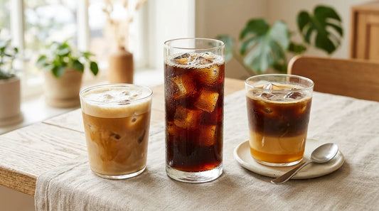 Three iced coffee drinks — cold brew, iced latte, and Vietnamese iced coffee — styled on a linen tablecloth in a bright home café setting