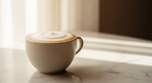 Thick velvety latte foam in a matte ceramic cup on a marble surface with soft natural light