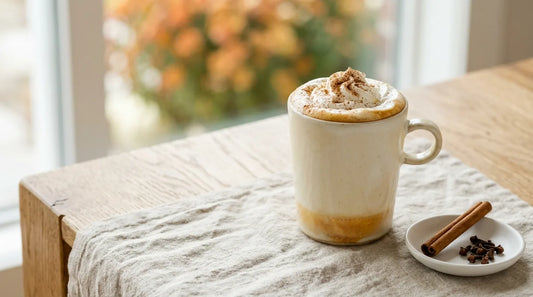Homemade pumpkin spice latte in a cream stoneware mug topped with whipped cream and cinnamon on a linen tablecloth